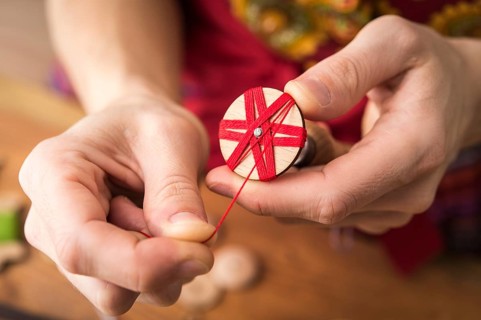 Button maker in third step of Posamentenknopfe production holding wooden blank with vise and carefully wrapping red yarn