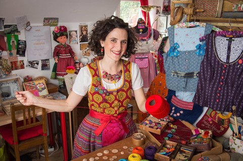 Button maker in colorful dirndl with Collier button trimmings in handicraft studio working with red yarn and utensils for Posamentenknopfe