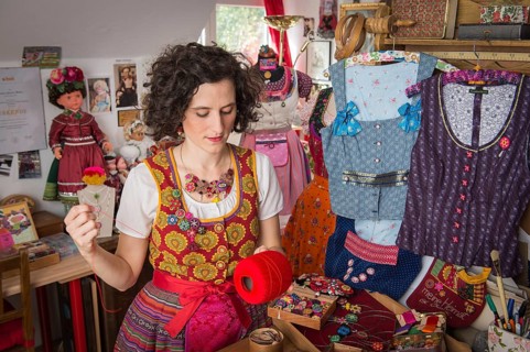 Button maker in colorful dirndl with Collier button trimmings in handicraft studio working with red yarn and utensils for Posamentenknopfe