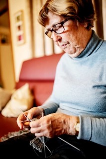 Senior knitting a stocking on the sofa at home