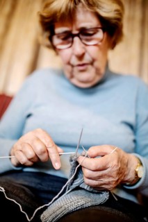 Senior knitting a stocking on the sofa at home