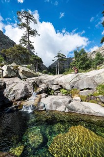 Young man sitting next to a pool with small waterfall in the mountains