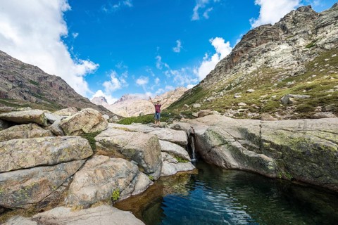 Young man standing next to a small waterfall with pool in the mountains