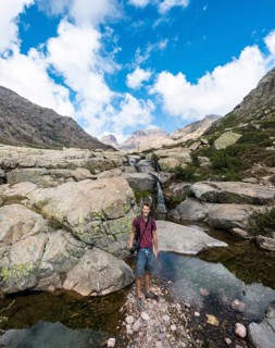 Young man standing at a pool with a small waterfall in the mountains