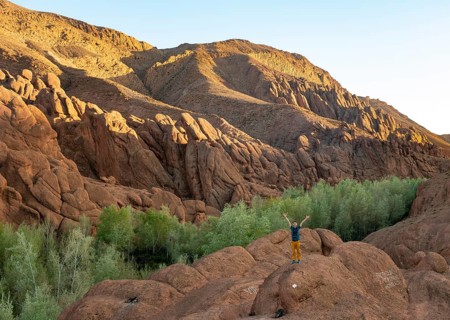 Young man stands on rock and stretches his arms into the air