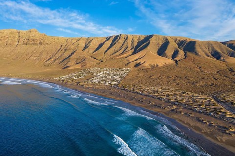 View on beach Playa Famara with bungalows and mountain range Risco de Famara