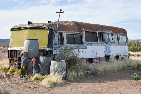 Boy and girl play at car wreck of an old bus