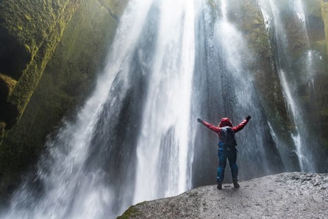 Hiker on rocks in front of Gljufrabui Waterfall in Hamragardar
