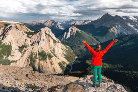 Female hiker with raised arms looking from summit over mountain landscape