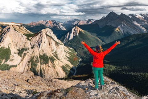 Female hiker with raised arms looking from summit over mountain landscape