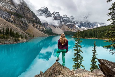 Young woman standing in front of a lake looking into mountain scenery
