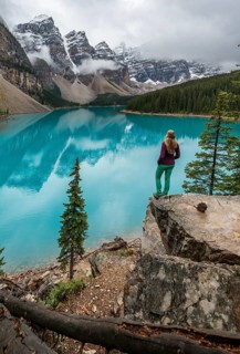 Young woman standing in front of a lake looking into mountain scenery