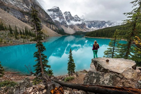 Young woman standing in front of a lake looking into mountain scenery