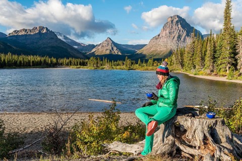 Young woman with breakfast at the mountain lake Two Medicine Lake in mountain landscape