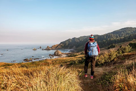 Young woman on a hiking trail along the rugged coast with many rocks