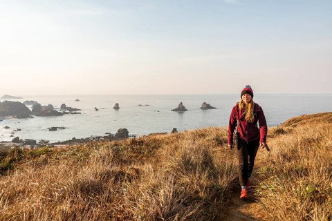 Young woman on a hiking trail along the rugged coast with many rocks