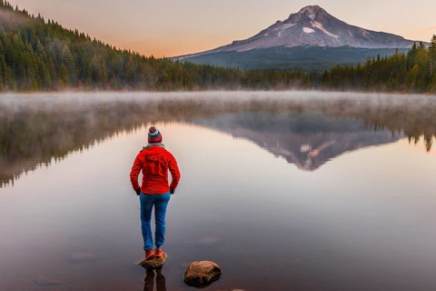 Young woman looking at view of volcano Mt. Hood with reflection in lake Trillium Lake