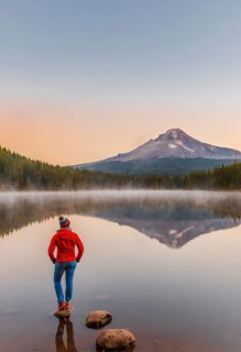 Young woman looking at view of volcano Mt. Hood with reflection in lake Trillium Lake