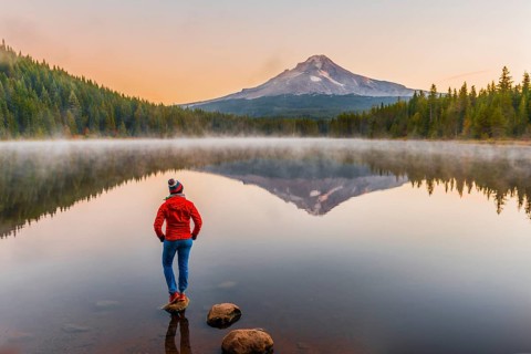 Young woman looking at view of volcano Mt. Hood with reflection in lake Trillium Lake