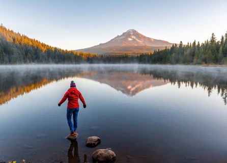 Young woman looking at view of volcano Mt. Hood with reflection in lake Trillium Lake