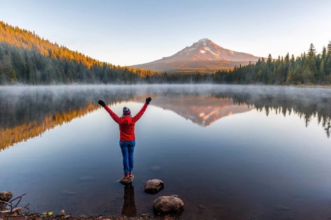 Young woman looking at view of volcano Mt. Hood with reflection in lake Trillium Lake