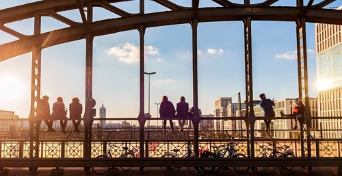 Young people sitting on the balustrade of the Hackerbrucke bridge over the railway tracks and looking into the distance