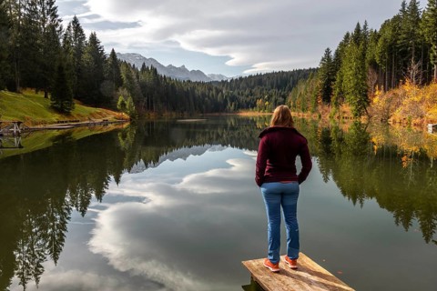 Female hiker stands on a footbridge and looks across the lake