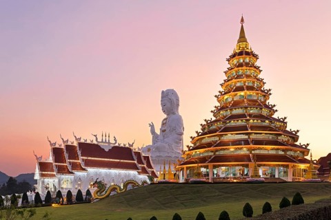 Nine-storey Chinese pagoda and chapel in front of huge Guan Yin statue at sunset
