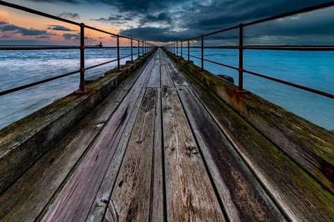 Old wooden jetty in the sea with dramatic clouds at sunset
