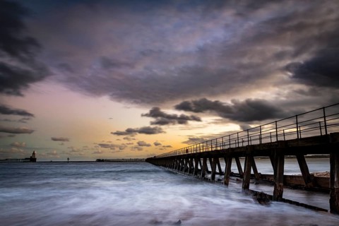 Bridge in the sea with dramatic clouds at sunset