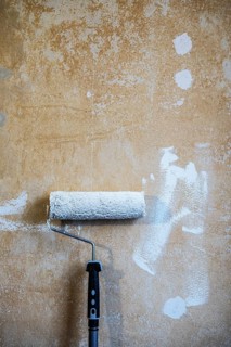 Painter's roller with white paint leaning against a plastered wall