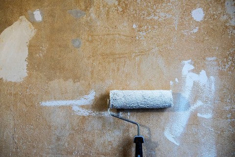 Painter's roller with white paint leaning against a plastered wall