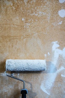 Painter's roller with white paint leaning against a plastered wall