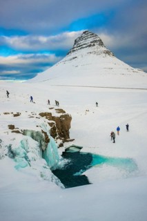 Tourists at the frozen waterfall Kirkjufellsfoss and the mountain Kirkjufell with snow