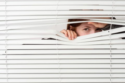 Young woman looking through blinds