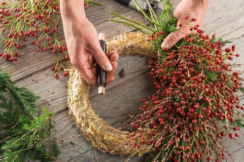 Autumn wreath on wood panel is bounded by hands with binding tool