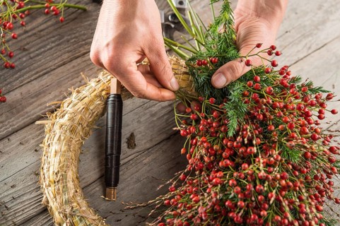 Autumn wreath on wood panel is bounded by hands with binding tool