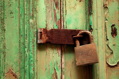 Rusty door lock with deadbolt on weathered wooden door with green paint