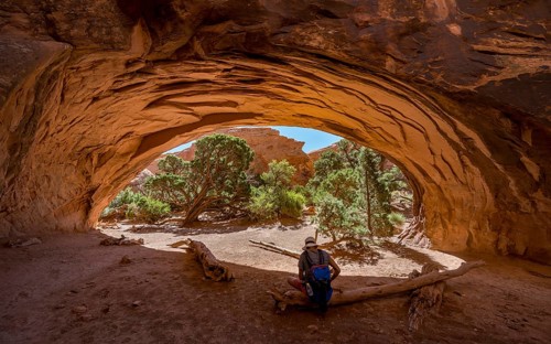 Young man sitting under rock arch