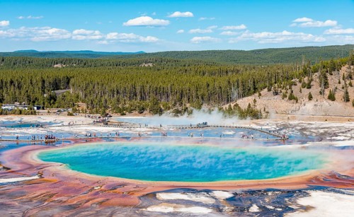 Visitors on footbridge over steaming hot spring with coloured mineral deposits