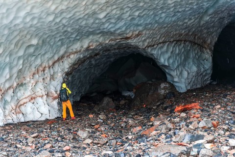 Man at the entrance of an ice cave of a glacier