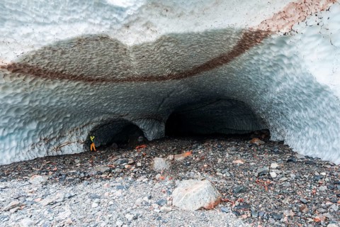 Man at the entrance of an ice cave of a glacier