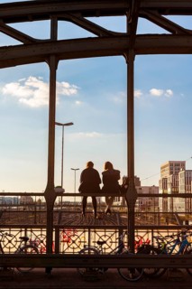 Two young women sitting on the balustrade of the Hackerbrucke bridge over the railway tracks looking into the distance