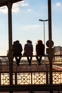 Three youths sitting on the balustrade of the Hackerbrucke bridge over the railway tracks looking into the distance