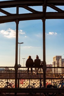 Two young women sitting on the balustrade of the Hackerbrucke bridge over the railway tracks looking into the distance
