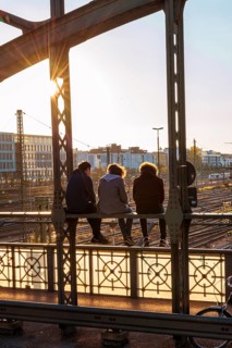 Three youths sitting on the balustrade of the Hackerbrucke bridge over the railway tracks looking into the distance