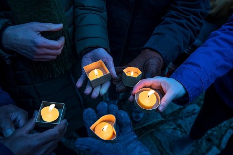 Hands holding devotional candles at dusk