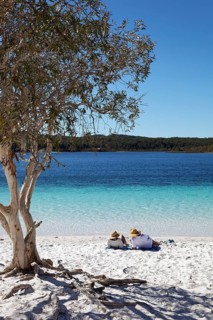 Couple lying on the sandy beach next to niaouli