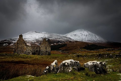 Rocks with white caps and house ruin in Highland landscape with snowy Cullin mountains in the background