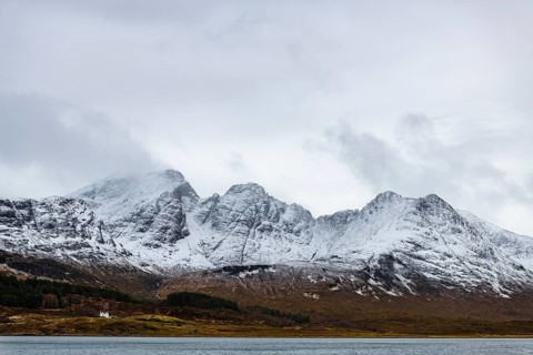Loch Slapin with small house in Highland landscape with snowy Cullin mountains in the background